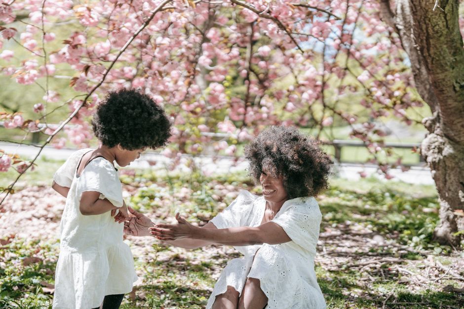 A joyful mother and daughter bonding under blooming cherry blossoms in a sunny park.