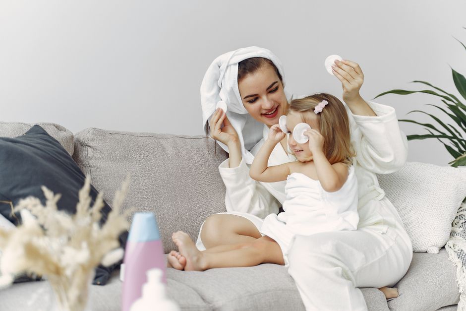 Mother and daughter in bathrobes enjoy bonding time on a cozy sofa, enhancing family togetherness.