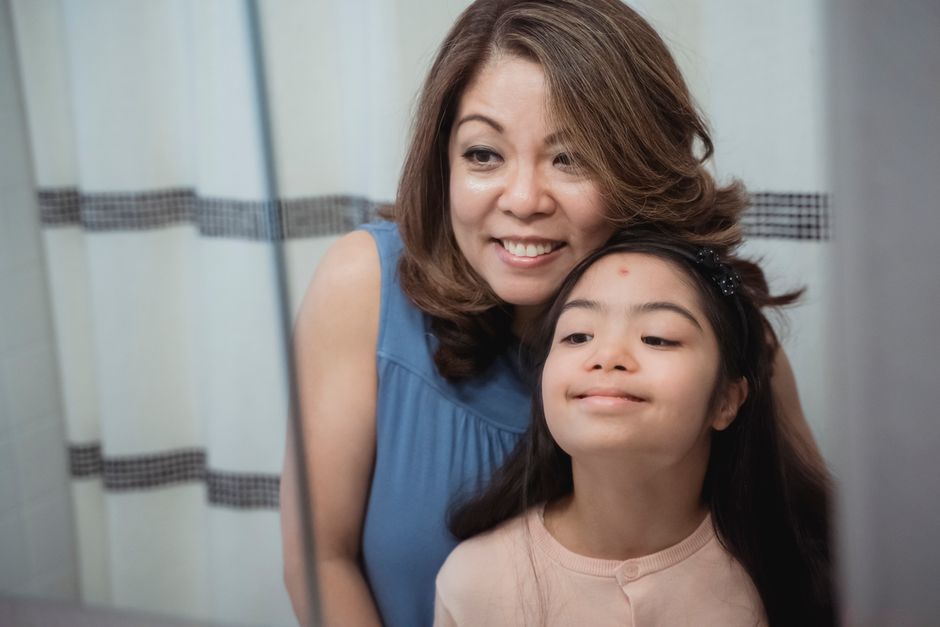 A joyful mom and daughter gaze together at their reflection, sharing a tender moment.